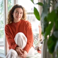 Девушка улыбается сидя на окне